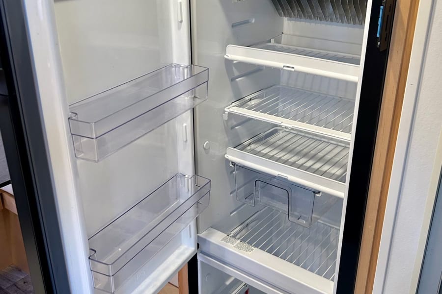 Inside a clean, open RV rental refrigerator: compact freezer, shelves, and door storage. Ready for your adventure!