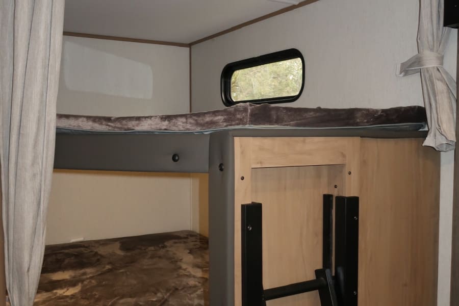 RV rental bunk beds: comfortable sleeping, privacy curtains on curved track, and ladder, perfect for family travel.