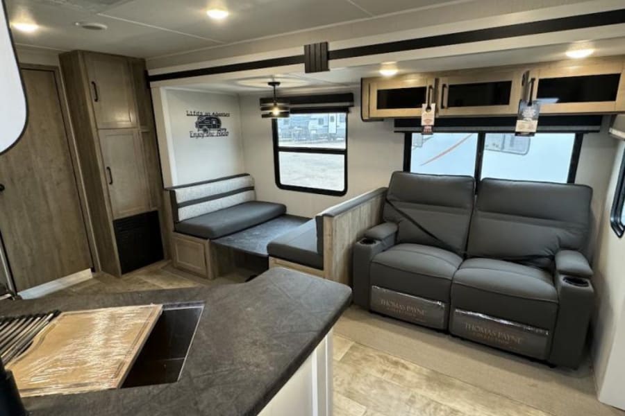 Modern RV rental interior with a cozy dinette, comfortable recliner sofa, and kitchen area. Ready for your travels!