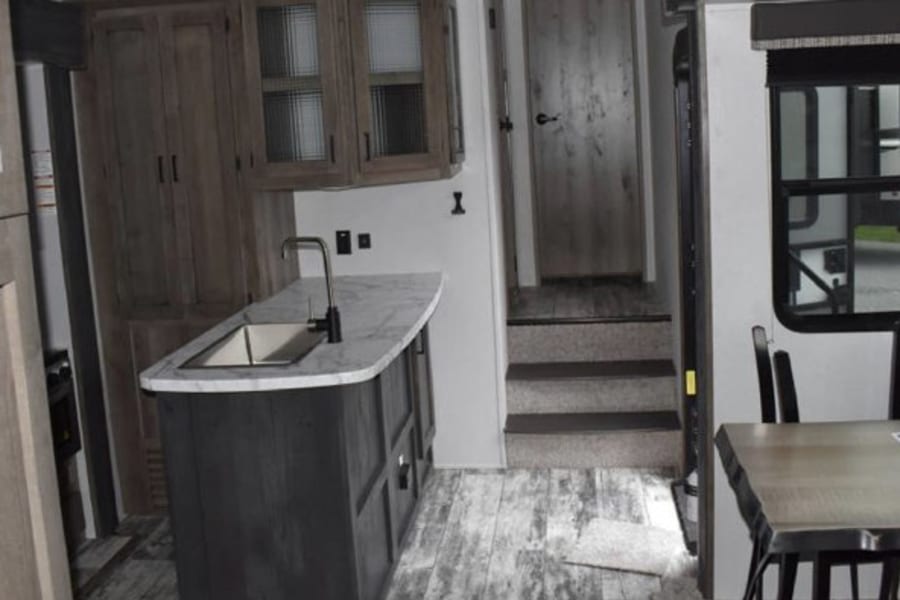 Modern RV rental interior: kitchen island, dining area, and steps leading to another section. Bright and spacious.