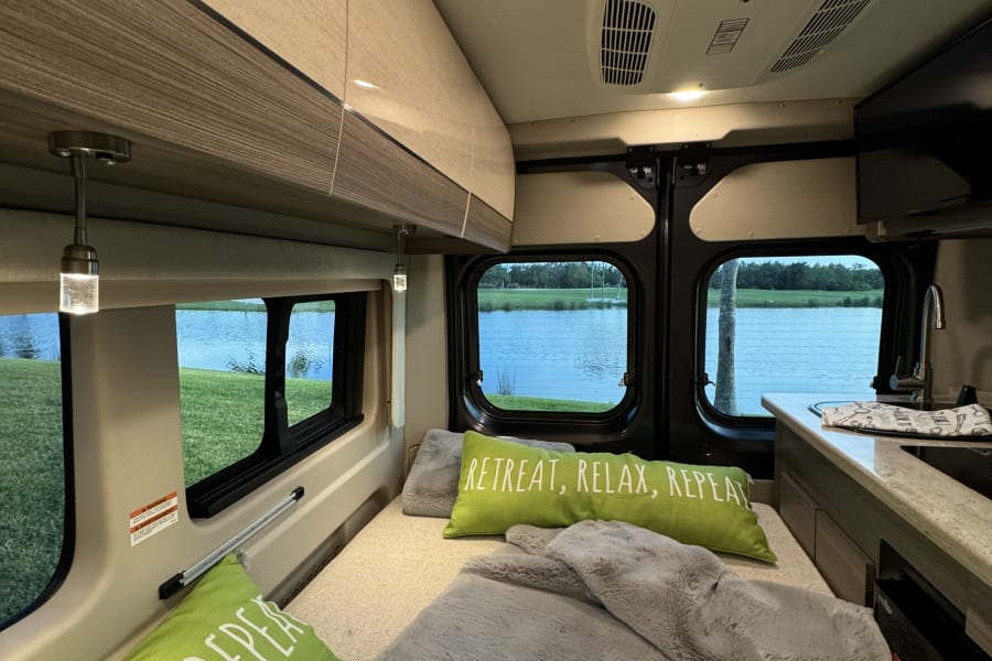This RV rental offers a cozy interior with a bed, lake views, kitchen area, & an AC unit for relaxing trips.