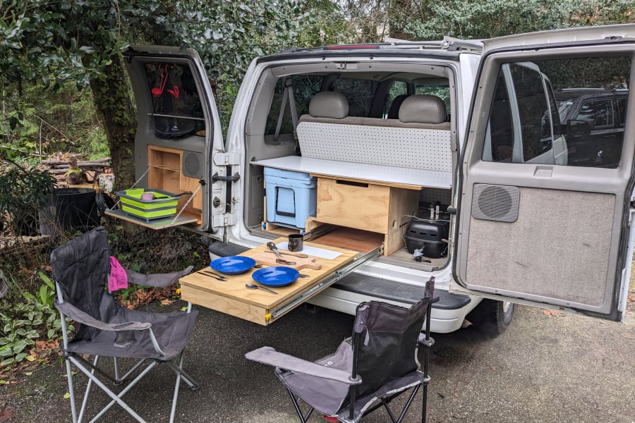 Van life rv rental: rear reveals a pull-out kitchen, cooler, and chairs for outdoor dining.