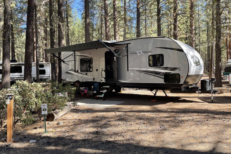 This RV rental is parked at campsite 48 in a sunny forest campground, ready for outdoor camping adventures.