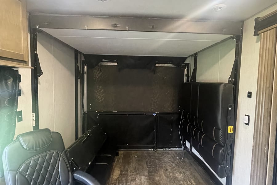 Spacious RV rental toy hauler interior featuring a comfortable recliner, versatile fold-up seating, and a large cargo area.