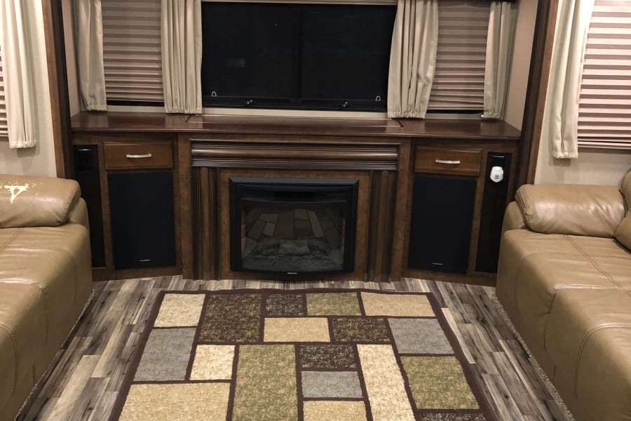 Spacious RV rental living area, featuring a cozy fireplace, entertainment center, and comfy sofas for your journey.