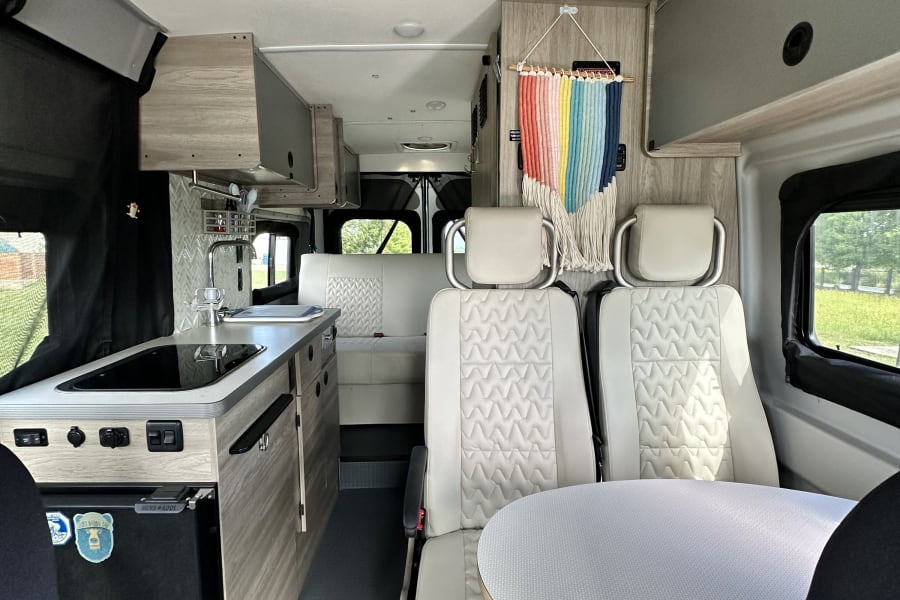 RV rental campervan interior featuring a compact kitchen, swiveling captain's chairs, and a round dining table.
