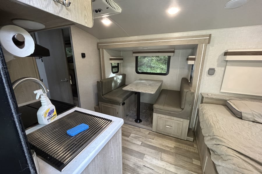 RV rental interior: cozy kitchen, dining booth, and bed area in a modern travel trailer with wood-look flooring.
