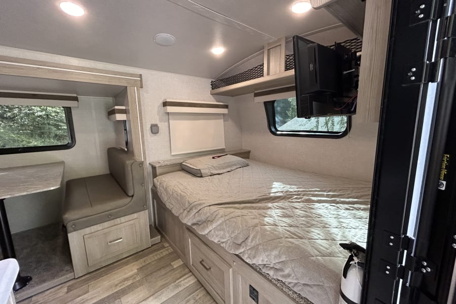 RV rental interior: bedroom with mounted TV, small dinette, and bright modern decor.