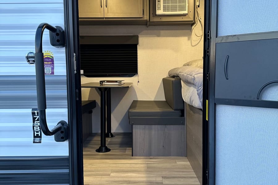 Inside a compact RV rental with a dinette, bed, and AC. Ready for adventure!