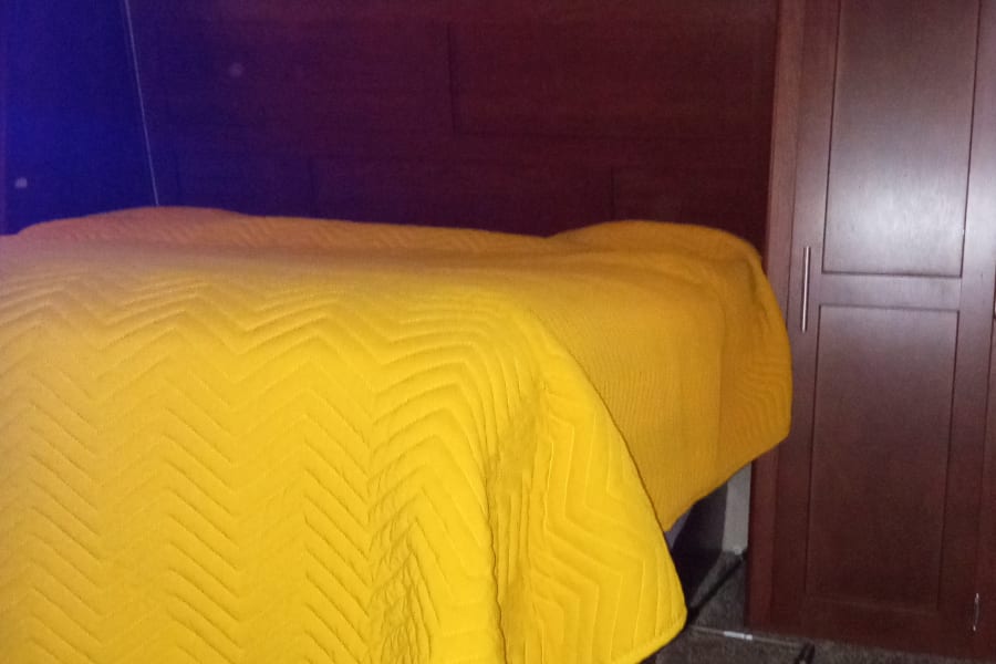 RV rental bedroom: yellow quilted bed, dark wood cabinets, carpeted floor. Compact & comfortable interior.