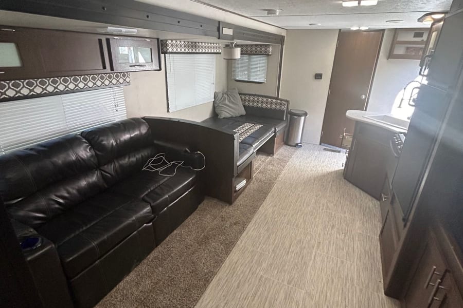 This RV rental features a comfortable black leather sectional sofa, dinette area, and functional kitchen with modern flooring.