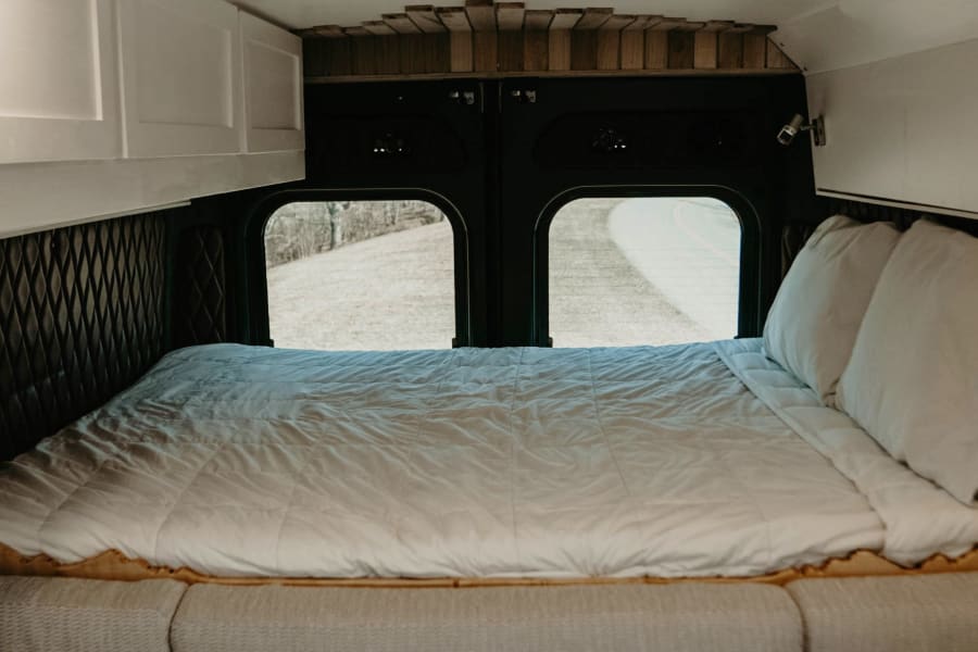 Spacious RV rental bedroom featuring a full bed, large windows, storage cabinets, and cozy seating. Ready for adventure!