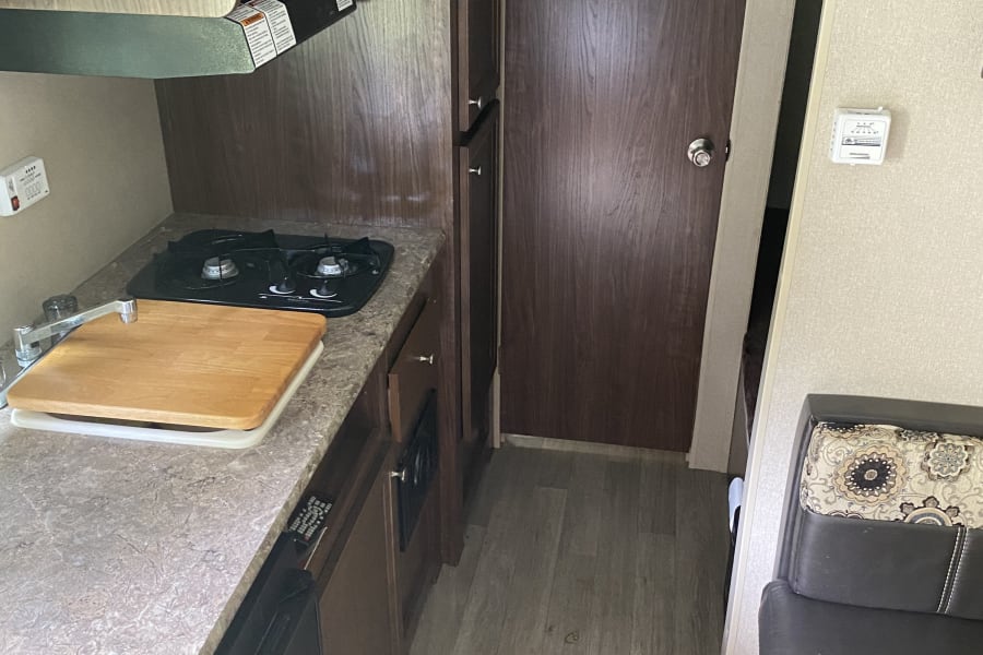 RV rental interior featuring a compact kitchen with microwave, stove, sink, and adjacent dinette seating.