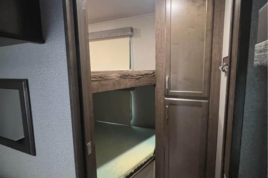 This RV rental's bright interior features cozy bunk beds and ample storage, creating a functional sleeping space.