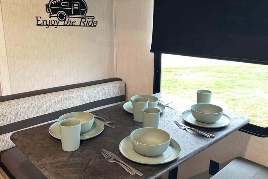 An RV rental's dinette features a table set with light green dishes, comfy benches, and adventure-themed decor.