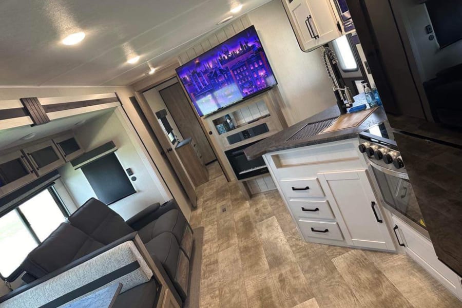 Step inside this modern RV rental: spacious living area with large TV, and a fully equipped kitchen.