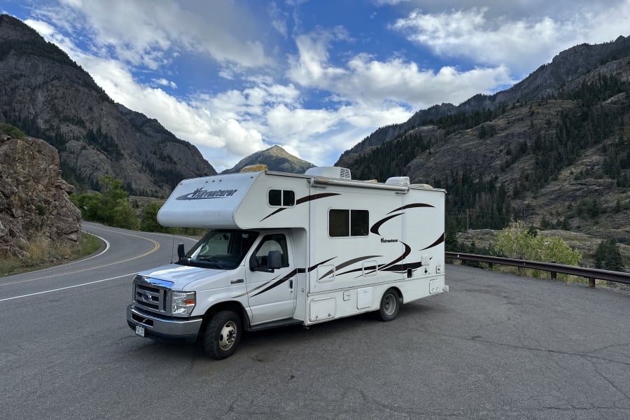 An Adventurer RV rental parked on a scenic mountain road, surrounded by majestic peaks and a partly cloudy sky. Ideal for adventure travel.