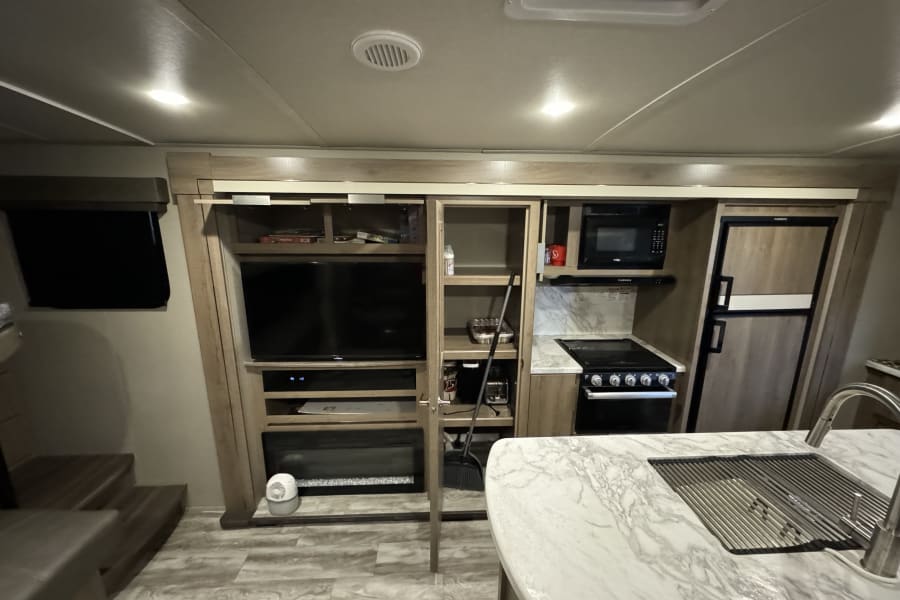 An RV rental's well-equipped interior: kitchen with sink, stove, fridge; living area with TV, fireplace & storage.