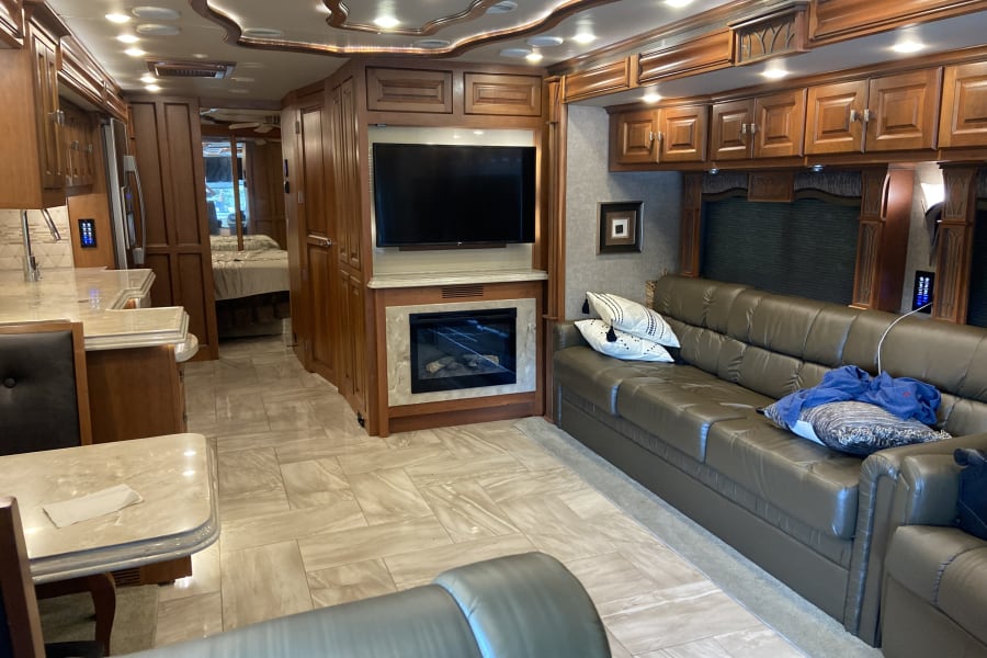 Explore this modern RV rental interior: comfortable living area with sofa, fireplace, TV; dining/kitchen space, and bedroom view.