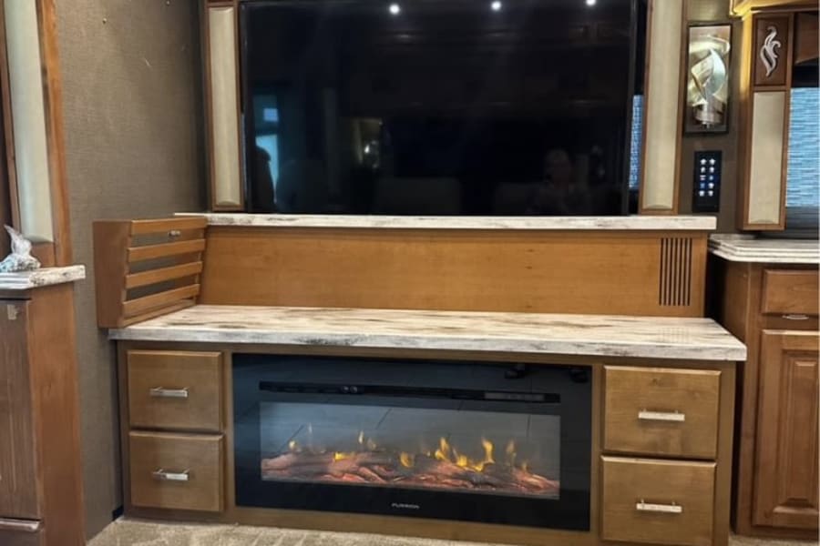RV rental: Spacious interior featuring a large TV, electric fireplace, and elegant wood cabinetry. Perfect for cozy relaxation.