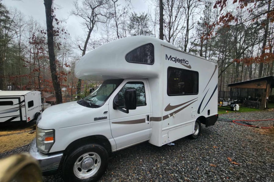 Majestic Ford E-350 Class C RV rental parked on gravel amid trees; ready for your outdoor adventure.