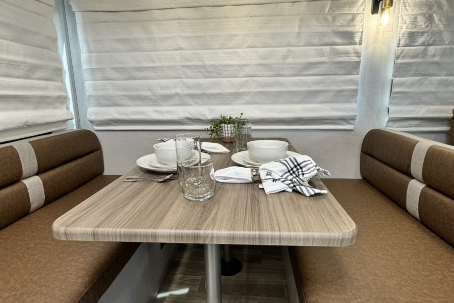 An RV rental's cozy dinette, featuring a wooden table, brown benches, and full place settings for meals.