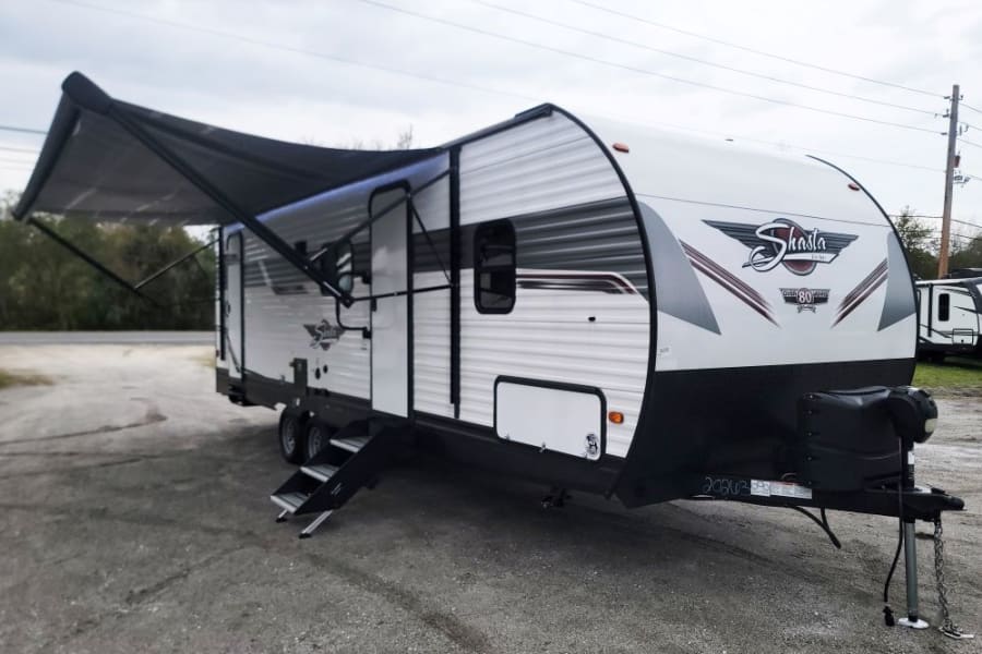 White Shasta travel trailer with an extended awning, ready for your RV rental adventure.
