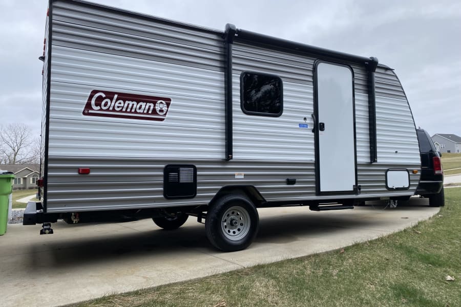 Silver Coleman travel trailer RV rental, ready for camping trips, parked on a driveway.