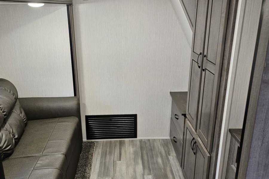 Inside an rv rental: a cozy living space with a grey sofa, light wood flooring, and sleek storage cabinets.