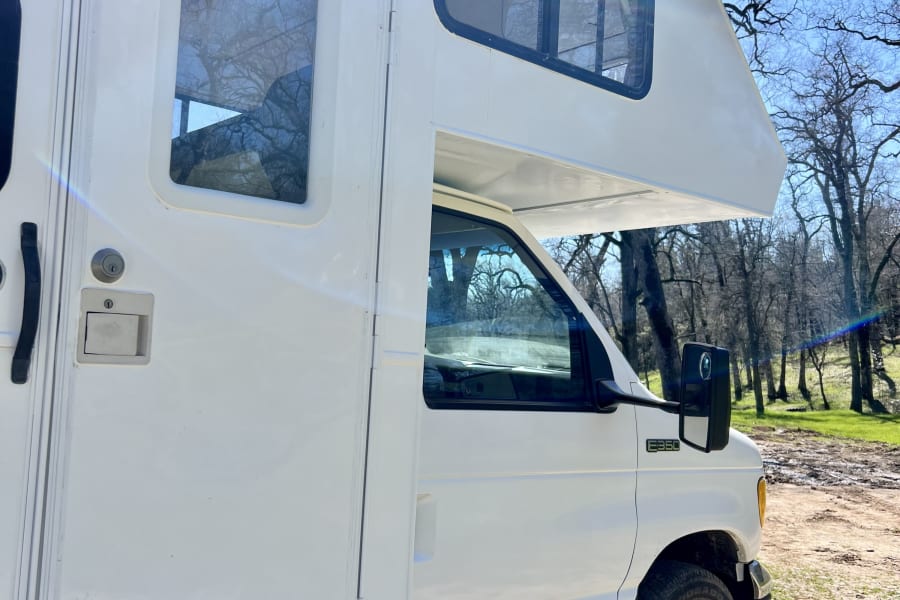 White Ford E350 RV rental, a campervan with an over-cab bunk, parked in a scenic outdoor setting under a clear sky.