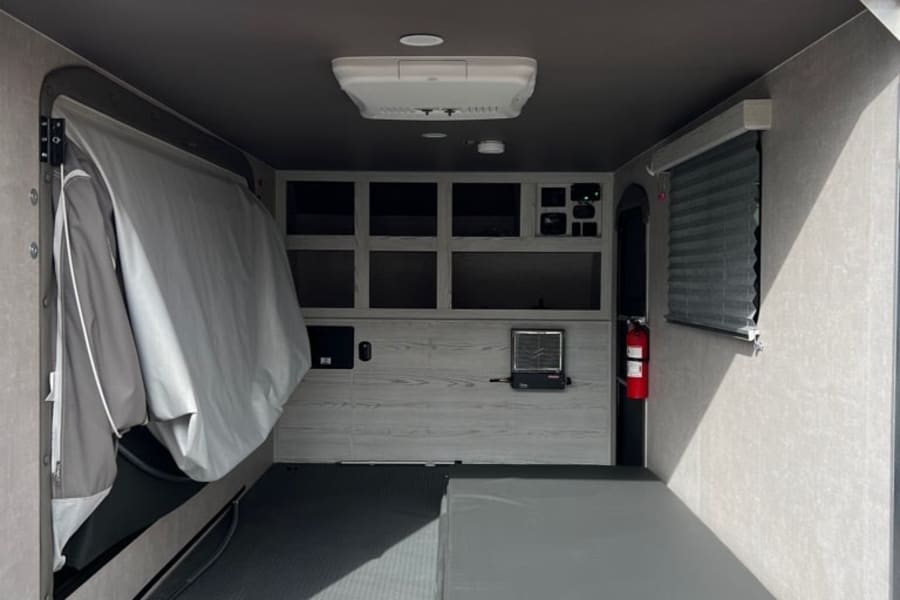 RV rental: View inside a functional camper/toy hauler, showing a fold-out bed, workstation, and durable floor.