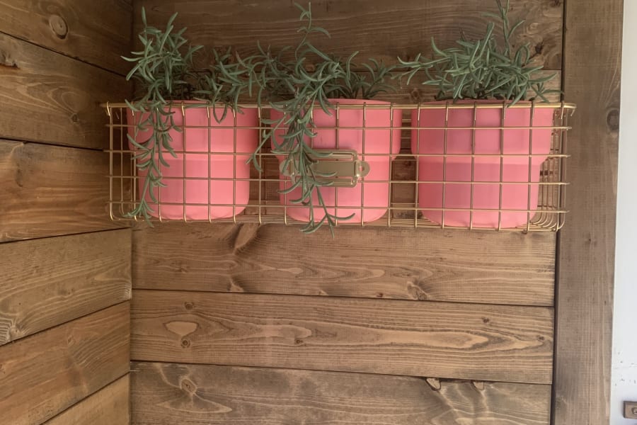 Cozy RV rental features pink potted plants in a gold wire basket on warm wood walls.