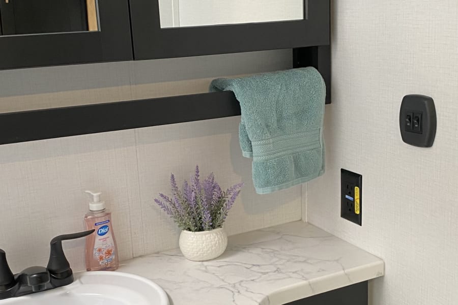 Modern RV rental bathroom: black vanity, white sink, marble counter, mirrored cabinet & organized essentials.