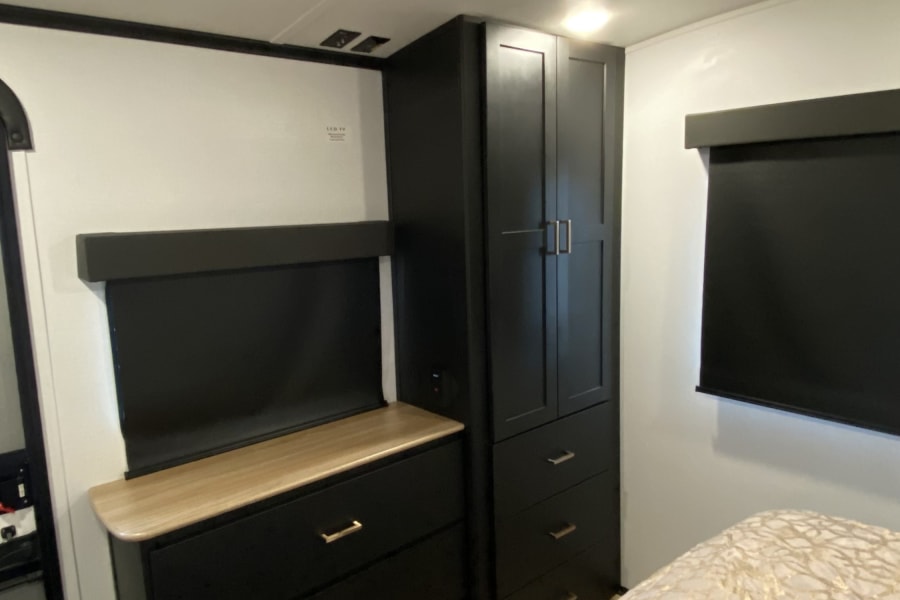 Cozy RV rental bedroom featuring modern black cabinetry, a light wood counter, patterned bed, and overhead AC.