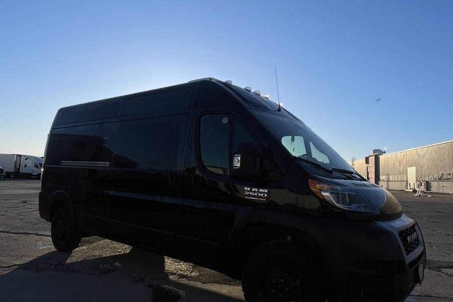 A sleek black Ram ProMaster van, perfect for rv rental, parked outdoors under a bright blue sky.