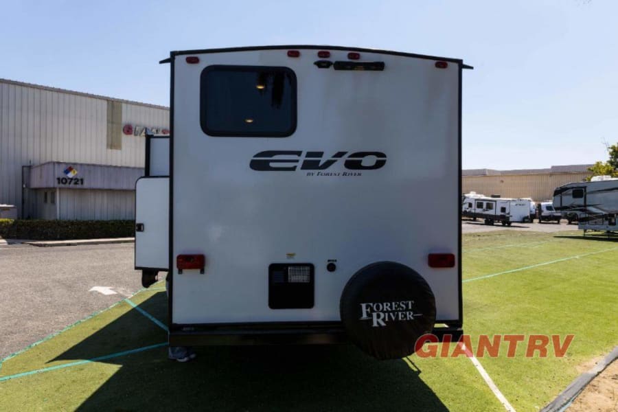 Rear view of a white Forest River Evo travel trailer, ideal for rv rental. Parked on artificial grass with a building behind.