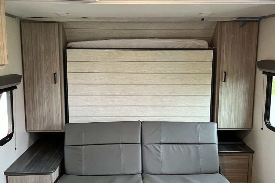 Inside an RV rental: a gray sofa, a wall-mounted bed, and ample storage cabinets.