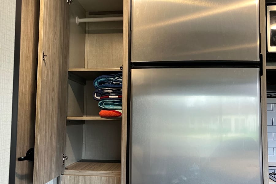 RV rental interior: stainless steel refrigerator, open cabinet with towels & drawers, and ceiling-mounted smoke detector.