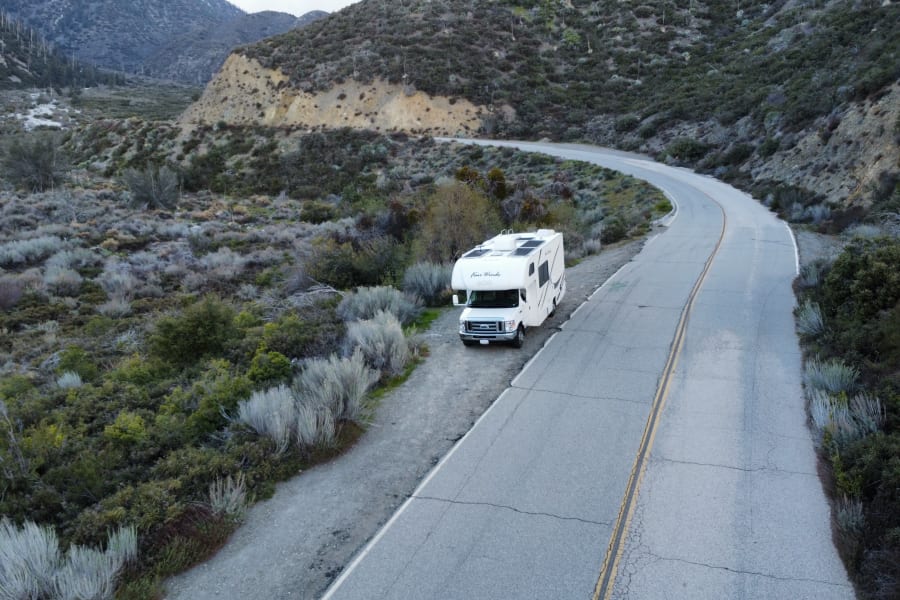 White RV rental parked on a mountain road's dirt shoulder. Winding road through scrubby hills, ready for adventure.