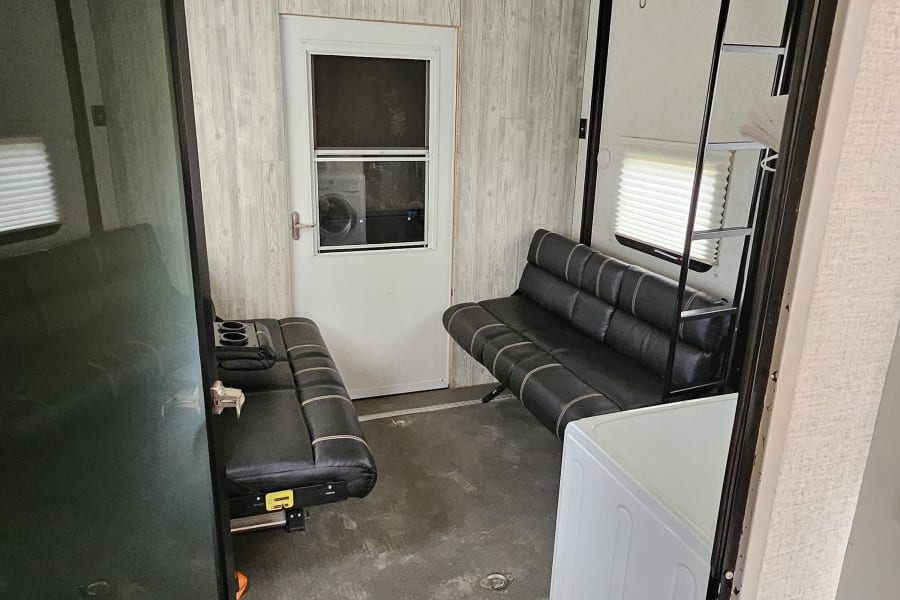 Spacious RV rental interior featuring convertible seating, a side door, rugged flooring, and a versatile layout.
