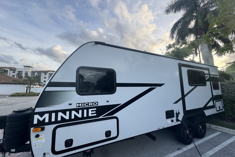 White Micro Minnie travel trailer, ideal for RV rental adventures. Parked outside with palm trees and buildings in view.