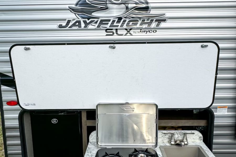 This RV rental features an outdoor kitchen with a fridge, two-burner stove, and sink, ideal for camping adventures.