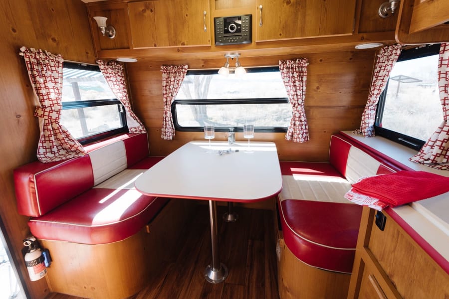 Step into this retro rv rental! Features cozy red and white diner-style seating, wood paneling, and a central table. Enjoy the view.