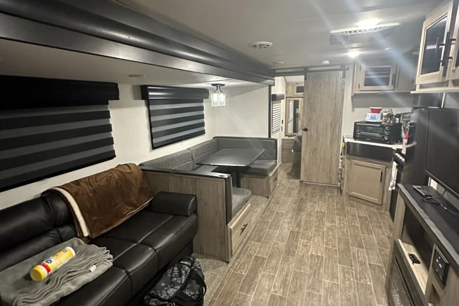 Bright RV rental interior featuring a sofa, dining booth, kitchen, and wood-look flooring. Ideal for road trips.