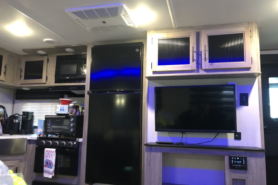 Cozy RV rental interior with a well-equipped kitchen (fridge, stove, microwave) and a living area featuring a TV and stereo.