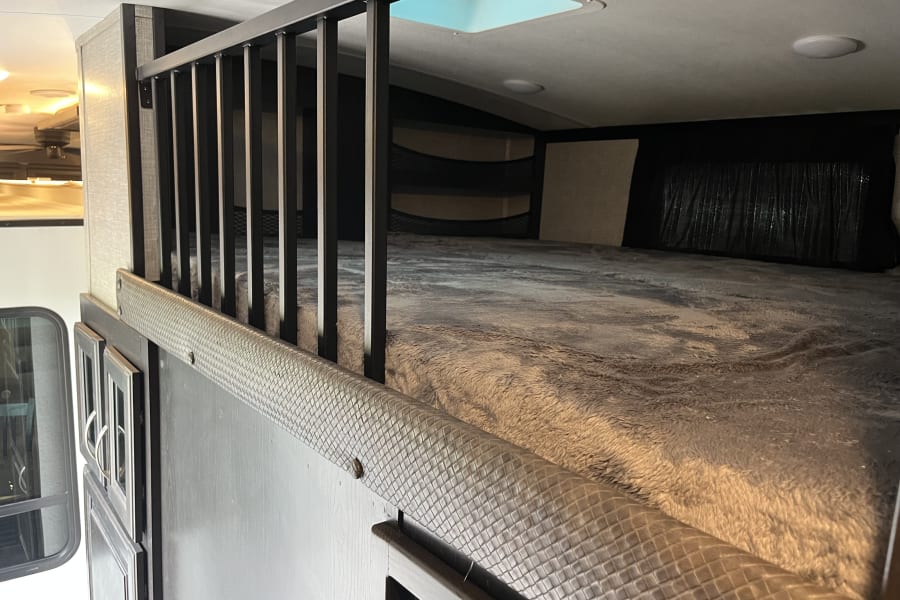 Cozy RV rental bunk bed/loft with a soft blanket, safety railing, and skylight, showing a comfortable sleeping area.