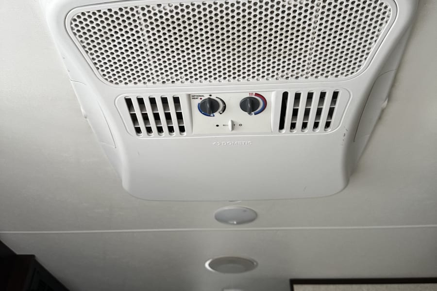 RV rental interior: A white Dometic RV air conditioner on the ceiling, with perforated grilles and climate control knobs.