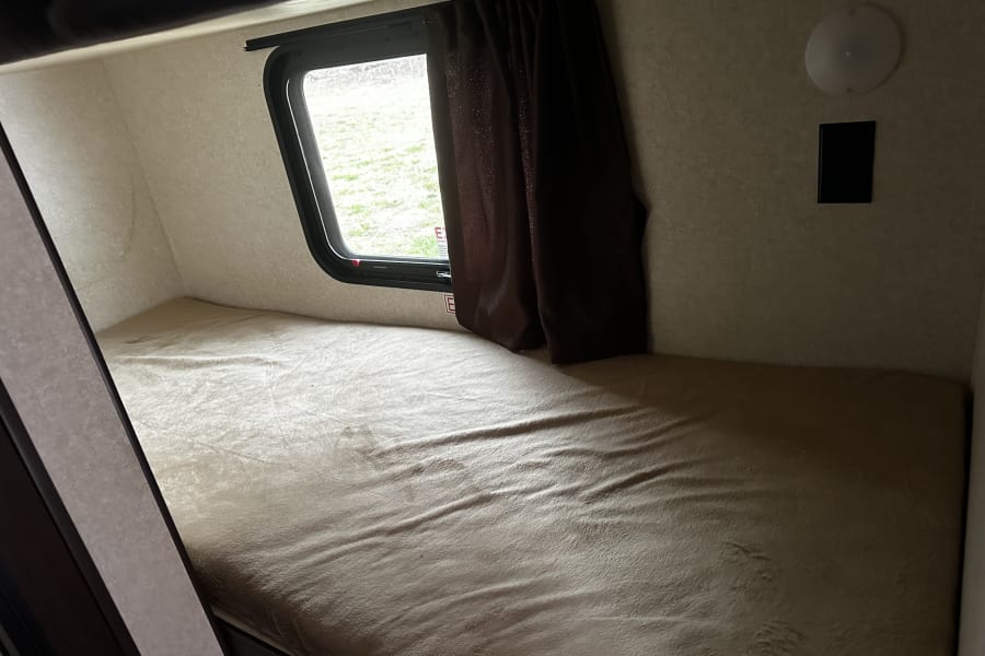 RV rental bunk bed: A compact, cozy bunk bed with a window, dark curtain, and light, offering comfort for travel.
