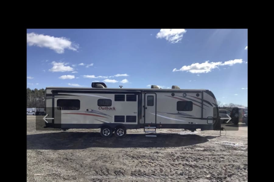Spacious beige Outback travel trailer RV rental with graphics, parked on a gravel lot under a sunny blue sky.