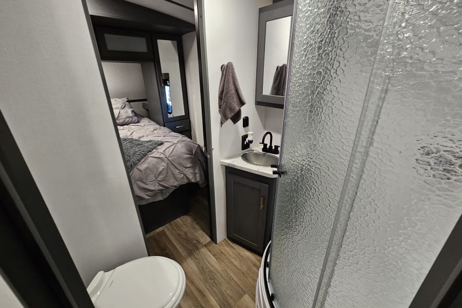 RV rental interior: compact bathroom with toilet, vanity, and shower, leading to a cozy bedroom.